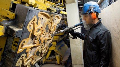 Técnico con casco y protector facial limpiando un gran molde de fundición para eliminar agentes desmoldantes sin necesidad de enfriar la máquina.